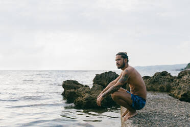 Mann sitzt am Strand am Rande des Wassers - CUF56225