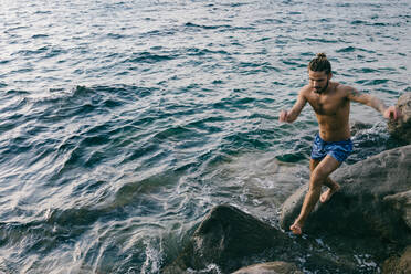 Man jumping from rock to rock in sea - CUF56237