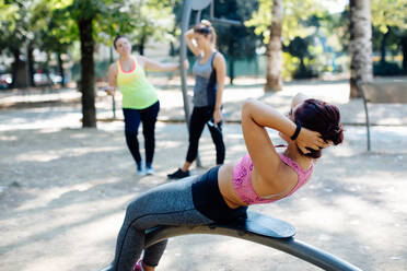 Woman doing sit ups in park, friends in background - CUF56239