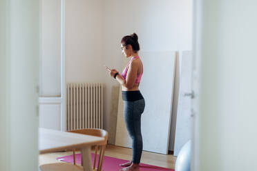 Woman doing exercise and texting at home - CUF56254