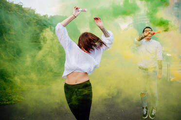 Mixed race group of friends hanging out together in town, using colourful smoke bombs. - CUF56301