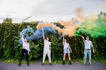 Mixed race group of friends hanging out together in town, using colourful smoke bombs. - CUF56304