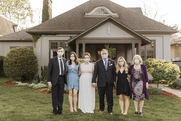 Wedding party posing for group portrait on front lawn, wearing face masks during Coronavirus crises. - ISF24264