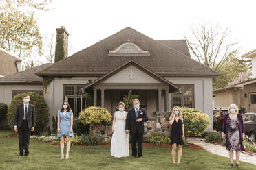 Wedding party posing for group portrait on front lawn, wearing face masks during Coronavirus crises. - ISF24265