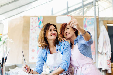 Zwei Frauen im Kreativstudio, die ein Selfie machen und ein Smartphone benutzen - CUF56332