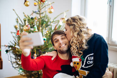 Ehepaar macht Selfie vor dem Weihnachtsbaum zu Hause - CUF56336