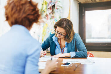 Zwei Frauen sitzen am Tisch und arbeiten in einer Kreativwerkstatt - CUF56350