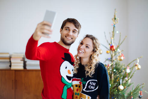 Ehepaar macht Selfie vor dem Weihnachtsbaum zu Hause - CUF56358