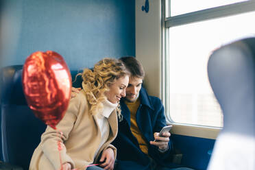 Paar mit herzförmigem Ballon und Smartphone im Zug - CUF56363