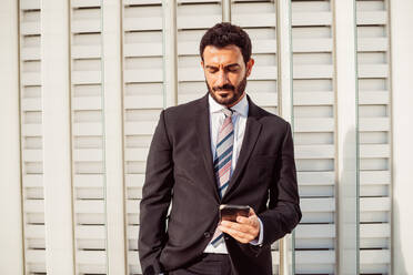 Portrait of bearded businessman wearing dark suit, checking mobile phone. - CUF56434