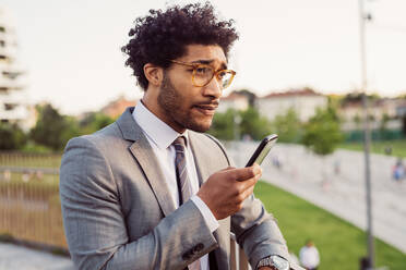 Porträt eines Geschäftsmannes mit Brille und grauem Anzug, der ein Mobiltelefon benutzt. - CUF56441