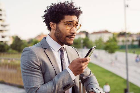Portrait of businessman wearing glasses and grey suit, using mobile phone. - CUF56441