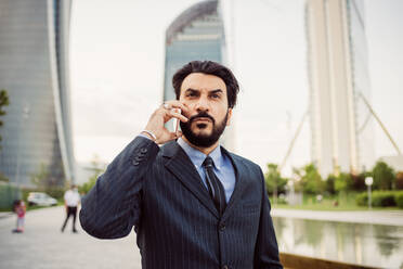 Portrait of bearded businessman wearing dark suit, using mobile phone. - CUF56448