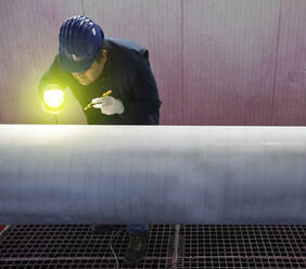 Ein Mann arbeitet in einem Stahlwerk und prüft ein Stahlrohr. - CUF56468