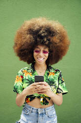 Smiling young woman using smartphone in front of green wall - JCMF01164