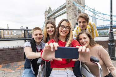 Glückliche junge Frauen und Männer machen ein Selfie mit der Tower Bridge im Hintergrund, London, UK - WPEF03274