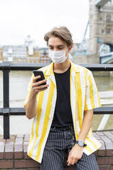 Mann trägt Gesichtsmaske, während er in der Stadt während des Ausbruchs des Coronavirus ein Mobiltelefon benutzt - WPEF03281