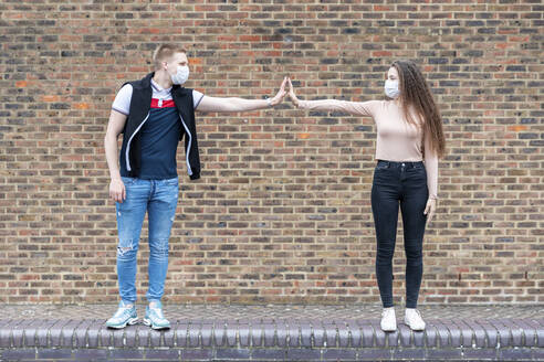 Male and female friends maintaining social distance while standing against brick wall - WPEF03291