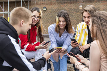 Cheerful male and female friends using smart phones while spending leisure time in city - WPEF03300