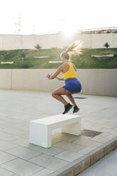 Junge sportliche Frau beim Training, die auf eine Bank springt - MPPF01040