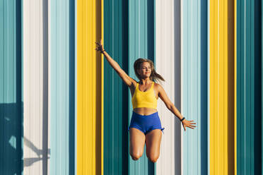 Blond athletic woman jumping in front of colorful wall - MPPF01045