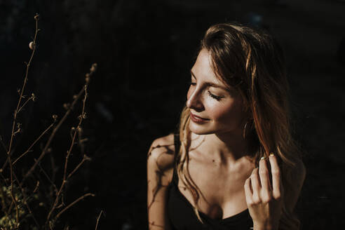 Thoughtful woman standing in sunlight - GMLF00440