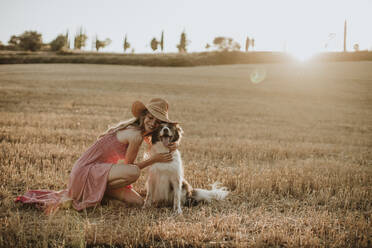 Woman embracing border collie dog in wheat field during sunset - GMLF00457