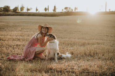 Border collie licking woman in wheat field during sunset - GMLF00458