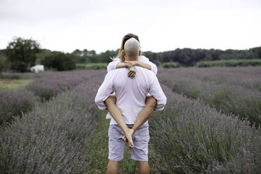 Rückansicht eines Mannes, der eine Frau auf einem Lavendelfeld hält - GMLF00498