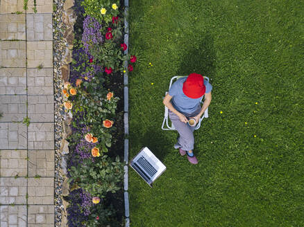 Woman sitting with laptop in garden - KNTF05255