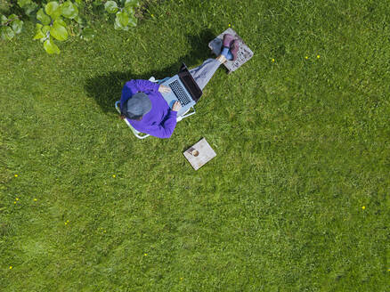 Woman using laptop in garden - KNTF05263