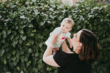 Mother picking up baby girl against ivy - EBBF00582