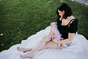 Frau schaut auf süße Baby-Mädchen schlafen auf ihrem Schoß, während sie in Hinterhof sitzt - EBBF00586
