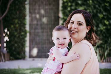 Happy mother carrying baby girl at back yard - EBBF00590