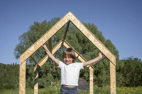 Glücklicher Junge hält Spielhausrahmen an einem sonnigen Tag - VPIF02845