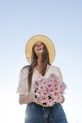 Lachende Frau steht und hält rosa Blumen gegen den klaren Himmel - RDGF00068