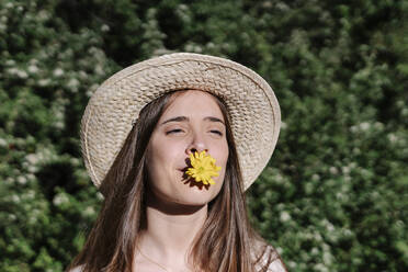 Junge Frau mit Hut und gelber Blume im Mund in einem Park im Frühling - RDGF00075