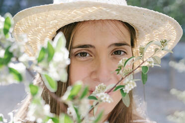 Schöne Frau mit Hut, die im Frühling durch die Blumen schaut - RDGF00076