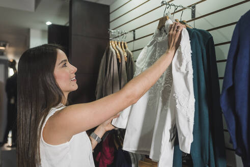 Happy young female customer choosing outfit for herself at store - DSIF00099