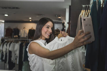 Lächelnde schöne Frau nimmt Selfie mit Outfit im Laden - DSIF00100