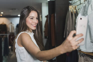 Lächelnde schöne junge weibliche Kundin nimmt Selfie im Laden - DSIF00102