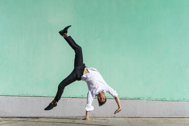 Geschäftsmann macht Handstand vor einer grünen Wand - AFVF06956