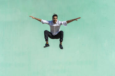 Businessman jumping in front of green wall - AFVF06957