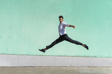 Businessman jumping in front of green wall - AFVF06958