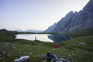 Clear sky over shore of Kogelsee lake at dawn with silhouette of lone camper standing in background - MALF00141