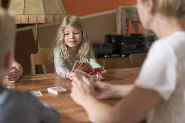 Cute blond girl playing cards with family at dining table - MOEF03085