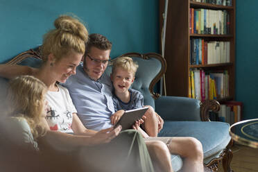 Family sharing digital tablet while sitting on sofa at home - MOEF03093