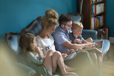 Familie schaut sich ein Fotoalbum an, während sie auf dem Sofa im Wohnzimmer sitzt - MOEF03096