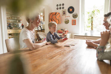 Familie spielt Karten, während sie am Wochenende am Esstisch sitzt - MOEF03099