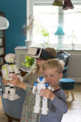 Cute siblings playing with toy robots and virtual reality simulator in living room at home - MOEF03108